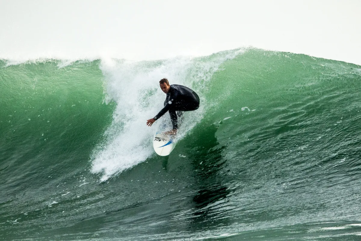 Simon accroupi sur sa planche en bas d’une vague creuse et verte, la lèvre au-dessus de lui.